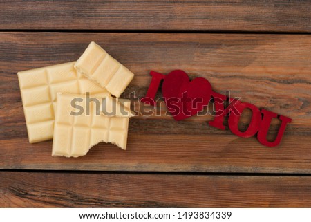 White chocolate pieces and inscription I love you. Chocolate bars and romantic message on wooden background.