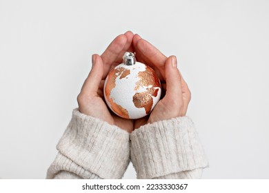 White Christmas ball in the form of a globe with a gold leaf holding carefully with two hands. The concept of caring for our planet. Solving problems in the new year. Hope and wish for peace on Earth. - Shutterstock ID 2233330367