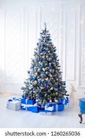 White Christmas Tree On White, Decorated With Blue Ornaments And Garland, Lots Of Presents Under The Tree