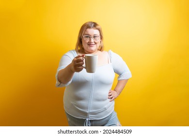 White And Chubby Young Woman Showing Cup Of Coffee. Overweight Person