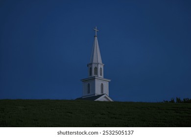 A white church steeple with a cross on top against a dark blue night sky - Powered by Shutterstock