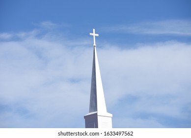 A white church steeple on a blue sky with white clounds 