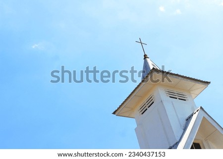 White church tower with cross against blue sky background in sunny weather