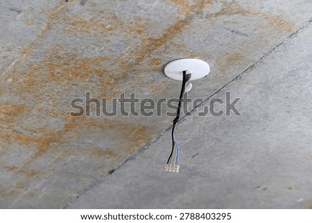 white circular ceiling mount with exposed multi-wire cable and connector, affixed to a grey concrete surface with visible rust stains and seams.
