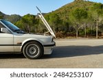 White Classic car broken down on the roadside, hood open, side view