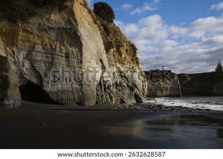 White cliffs at a New Zealand beach rise sharply from the sand, their surfaces marked by natural striations—layered bands of earth and stone etched by time and sea into the bright rock face.