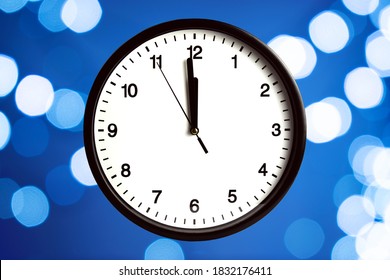 The white clock shows five seconds to midnight, with a bokeh background. Countdown to the New year - Powered by Shutterstock