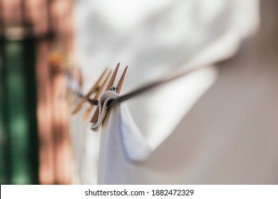 White clothes hanging on a clothesline with wooden clothespins. The clamp is in focus, the rest is out of focus. A window with black bars can be seen in the background. - Shutterstock ID 1882472329