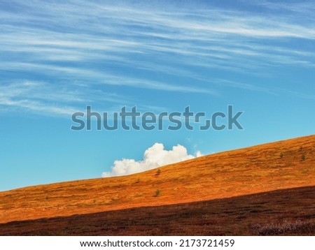White cloud goes behind the mountain. Autumn slope mountain and light sky. Minimal nature background with silhouette of mountain under blue sky.