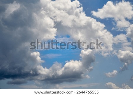 A white cloud with a round opening in the blue sky close-up, a view among clouds high in the sky with a round opening like a portal, clouds close-up, airy white clouds of whimsical shapes.