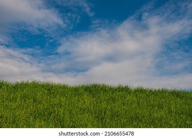 White clouds in the blue sky and green grass on the slope, rural landscape. Spring season, April.