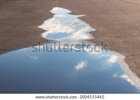 White clouds and sky are reflected in a puddle on the asphalt on the road.