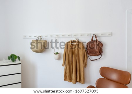 White coat-rack with basket, plant, coat and armchair