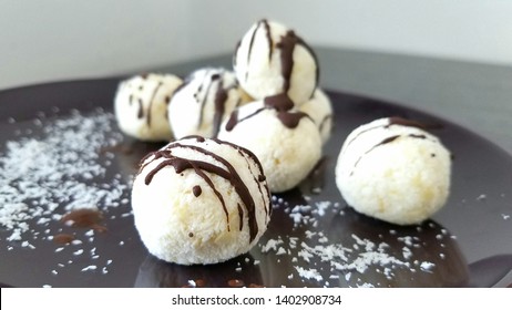 White coconut and almonds dessert balls with dark chocolate decoration stacked on brown plate.