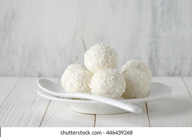 White coconut candy balls in plate on rustic wooden background. White food styling.