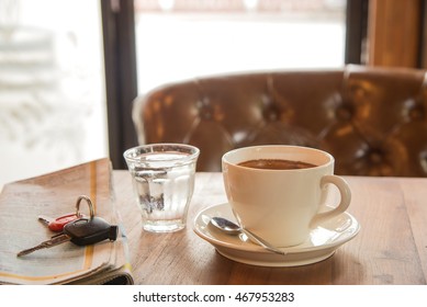 White coffee cup , blurred newspaper , car key and glass water on wooden table.blur background with back lighting.