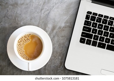 white coffee cup with laptop computer or notebook isolated on cement background