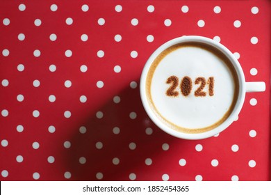 White coffee cup with the number 2021 over frothy surface on red and white polka dots background. Holidays food art creative theme for active days in New Year 2021. (top view, space for text) - Powered by Shutterstock