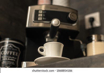 White Coffee Cup With Saucer On Kitchen Table With Modern Coffee Machine At Background. Modern Coffee Station At Home