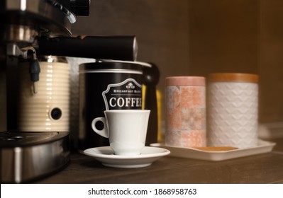 White Coffee Cup With Saucer On Kitchen Table With Modern Coffee Machine. Modern Coffee Station At Home