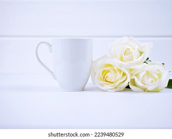 White coffee mug mockup with s bouquet of rose flowers on a white table background ,Blank copy space for text or design Valentine's Day concept Empty mug mock up Template layout Advertising 