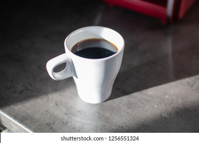 White Coffee Mug And Red Coffee Machine In The Morning Light On A Concrete Counter Top.