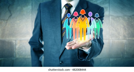 White Collar Manager Presenting A Work Team Of Five Multicolored Worker Icons In Open Palm Of His Left Hand. Business Concept For Team Building, Diversity Inclusion Culture And Staffing Solutions.