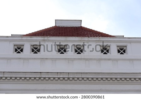 White colonial building upper facade with decorative cross ventilation windows dentil cornice and red terracotta tiled roof.
