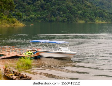 A white colored speed boat with the blue canopy is parked near the pier on the shore of a tranquil lake surrounded by lush green dense tropical evergreen mountain forests, Shillong, Meghalaya, India - Powered by Shutterstock