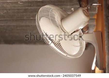 A white colored Wall revolving fan or table fan on an orange wall in background