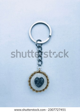 A white colour circle shape keytag on white beautiful. It has only one small black heart and it has silver colour keychain and gold colour border. It is made of resin material. It is beautiful.