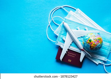 a white comercial airplane  above some mask for covid-19 and a red passport book
