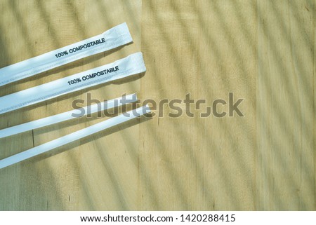 White compostable straws with packaging with 100% Compostable wording printed on wooden background. Stop plastic pollution. Ecologically friendly.