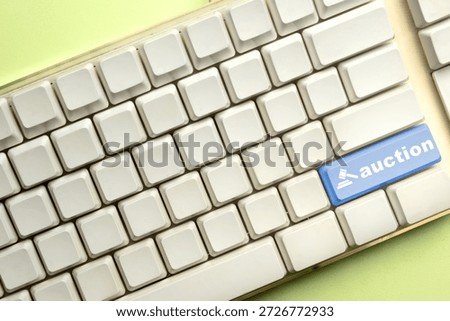 A white computer keyboard featuring a prominent blue 'auction' key with a gavel icon, symbolizing online bidding, digital sales, and internet-based commercial transactions