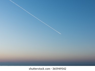 White Condensation Trail From an aeroplane flying across a beautiful blue and pink sunset sky