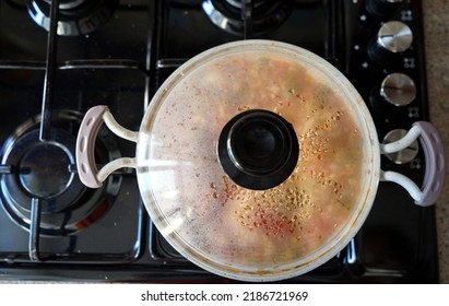 White Cooking Pot On The Oven, Pan Lid, Meal Is Cooking, Top View, Black Stovetop.