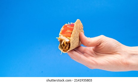 White Corn Tortilla Angled In Hand On Blue Background