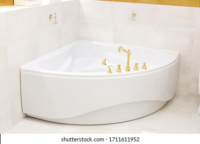 White corner bath, whirlpool. Golden faucet, faucet on the bathroom. Golden hooks on the wall. The interior of the bathroom