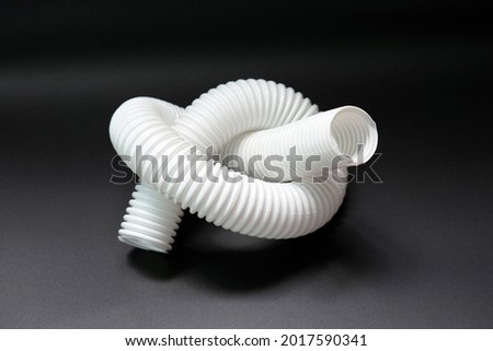 White corrugated sewer hose tied in a knot on a black background. Sewerage problem concept, shutting off the water