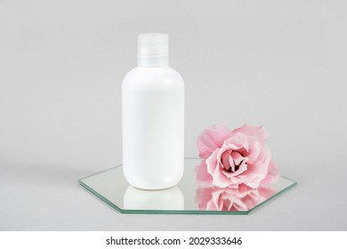 White Cosmetic Blank Bottle And Pink Flower On Mirror, Gray Background. Natural Organic Spa Cosmetic Beauty Concept Mockup, Front View.