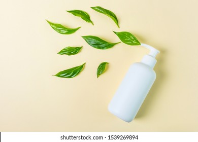 White cosmetic bottle with dispenser on a beige background. Near the dispenser are fresh green leaves. Concept of eco friendly cosmetic, cruelty free. Minimalism, place for text.