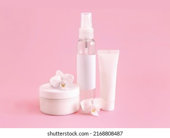 White cosmetic jar, tube and bottle near white orchid flower on light pink, close up, mockup. Skincare beauty product, cream or lotion. Exotic natural cosmetics, pastel minimal composition