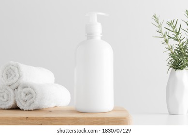 White Cosmetic Liquid Soap Dispenser Bottle Mockup With Towels And A Rosemary On A Wooden Table.