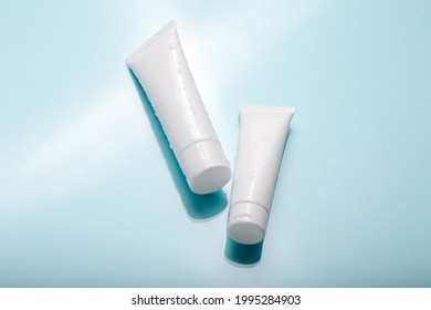White cosmetic product in tubes on color background with water drops. Mock up skincare cosmetic package on blue. Water balance cosmetic product