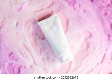 White Cosmetic Tube On A Pink Background With Soap Foam And Bubbles. Face Or Body Cleanser Concept. 