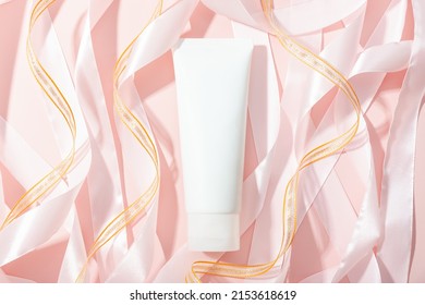 White Cosmetic Tube, Roll Pink And Gold Ribbons On Pink Background, Mockup. Daily Cream, Gel, Skin Care, Sunscreen, Moisturizer. Front Top View, Blank Bottle. Flat Lay.