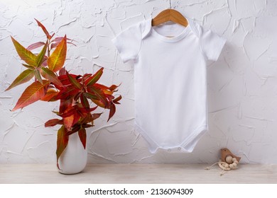 White cotton baby short sleeve onesie mockup with red fall grass in the vase and wooden bird toys. Design gender neutral bodysuit template, newborn romper print presentation mock up