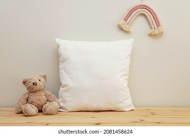 White cotton square baby girl pillow mockup for design presentation, minimal composition on wooden shelf with toy bear and boho rainbow wall decoration.
