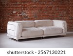 A white couch sits in front of a brick wall. The couch is large and has a white fabric covering. The brick wall behind the couch is red and has a rough texture. Scene is cozy and inviting