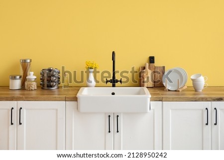 White counters with sink, kitchen utensils and food near yellow wall